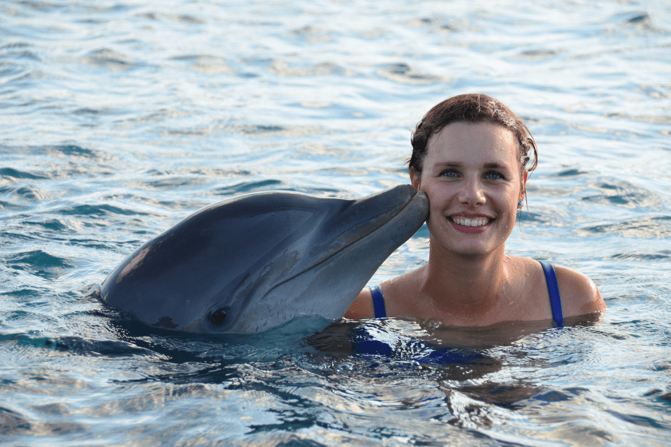 Dolfijn geeft vrouw kus op wang terwijl zij in de camera kijkt